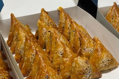 Assortiment de feuilletés triangulaires dorés, garnis de graines de sésame, présentés dans une boîte ouverte.