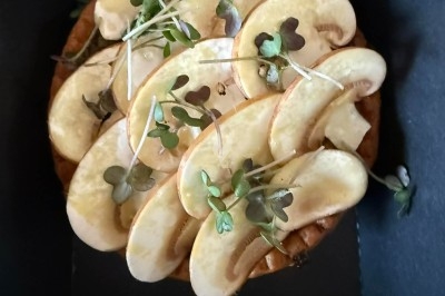 Tarte garnie de fines tranches de champignons frais et de jeunes pousses, présentée dans une boîte noire.