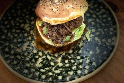 Burger garni de viande effilochée, salade et graines sur un pain, présenté sur une assiette décorative.