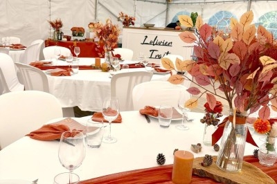 Tables décorées dans une tente, ornées de feuilles d'automne, bougies et nappes rouges pour un événement festif.