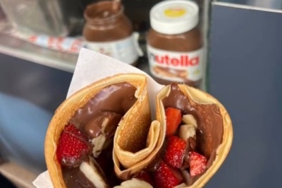 Crêpe garnie de chocolat, fraises et bananes, tenue à la main devant un pot de pâte à tartiner.