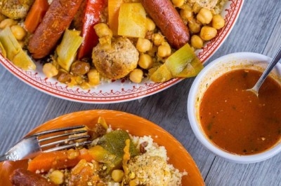 Assiette de couscous garnie de légumes, merguez, boulettes et pois chiches, accompagnée de sauce rouge.