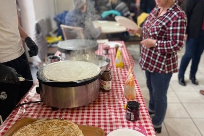 Un stand de crêpes avec un cuisinier en action et une femme attendant, dans une salle animée.