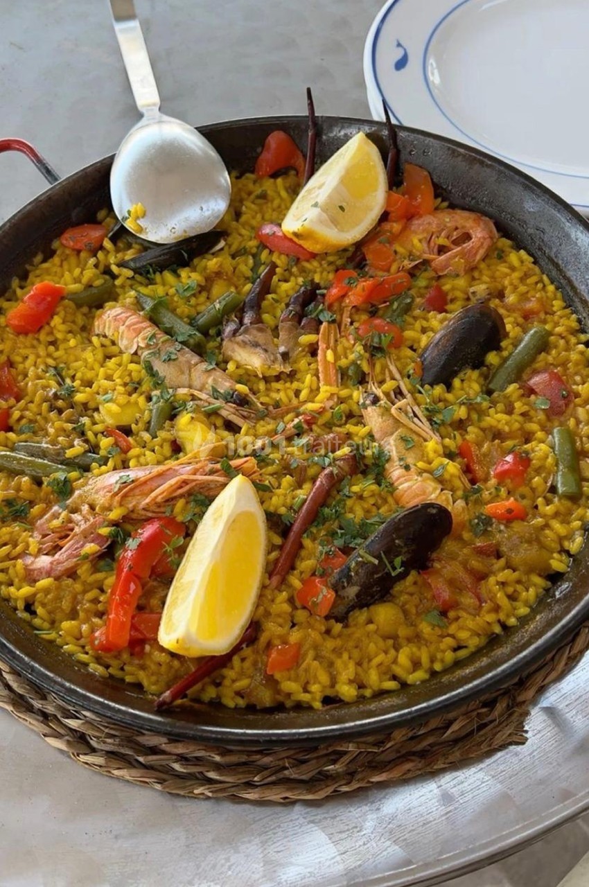 Plat de paella aux fruits de mer avec crevettes, moules, légumes et quartiers de citron dans une poêle en fonte.