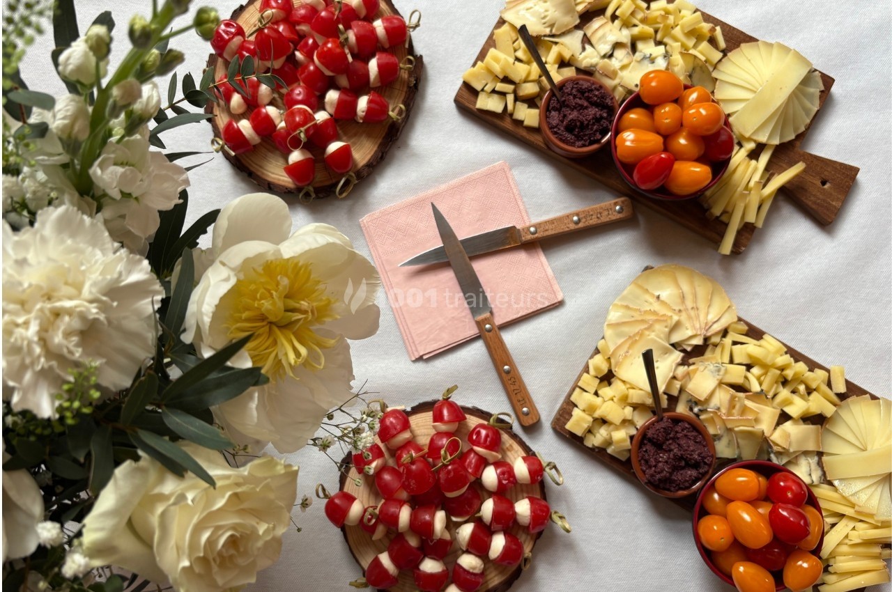 Plateaux de fromages, tomates cerises et olives, disposés sur une table avec des fleurs blanches en décoration.