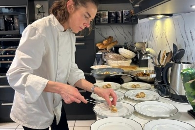 Une cheffe en cuisine dispose des amuse-bouches sur des assiettes blanches alignées sur un plan de travail.