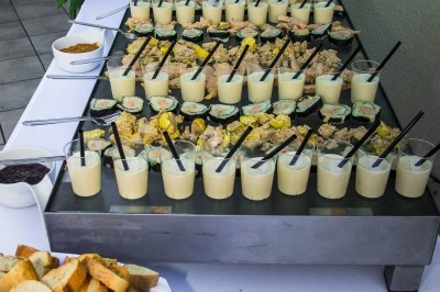 Buffet avec verrines salées garnies de cuillères, accompagnées de pain grillé et de condiments sur une table blanche.