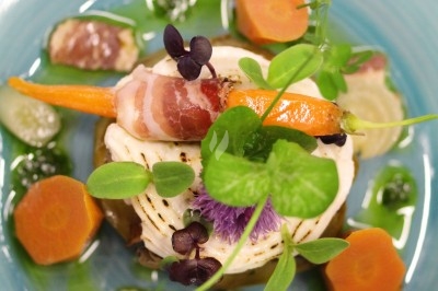 Assiette gastronomique composée de légumes colorés, d'herbes fraîches et d'une garniture enroulée de lard.