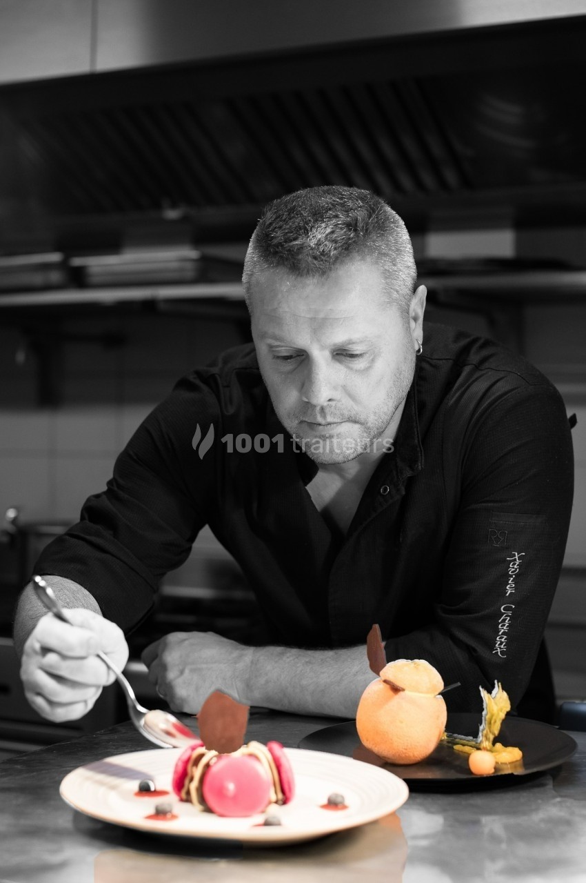 Un chef pâtissier décore un dessert coloré dans une cuisine professionnelle.