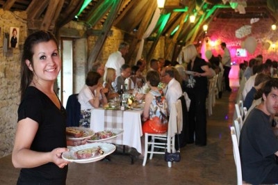 Une serveuse souriante apporte des plats dans une salle de réception animée avec des invités attablés.