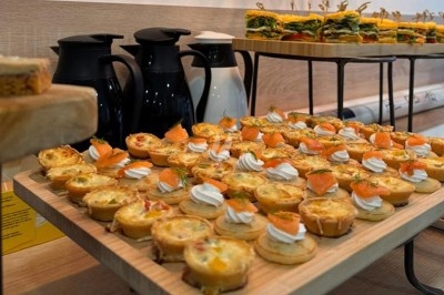 Plateau de bouchées salées variées, incluant des quiches et des toasts au saumon, avec des carafes en arrière-plan.