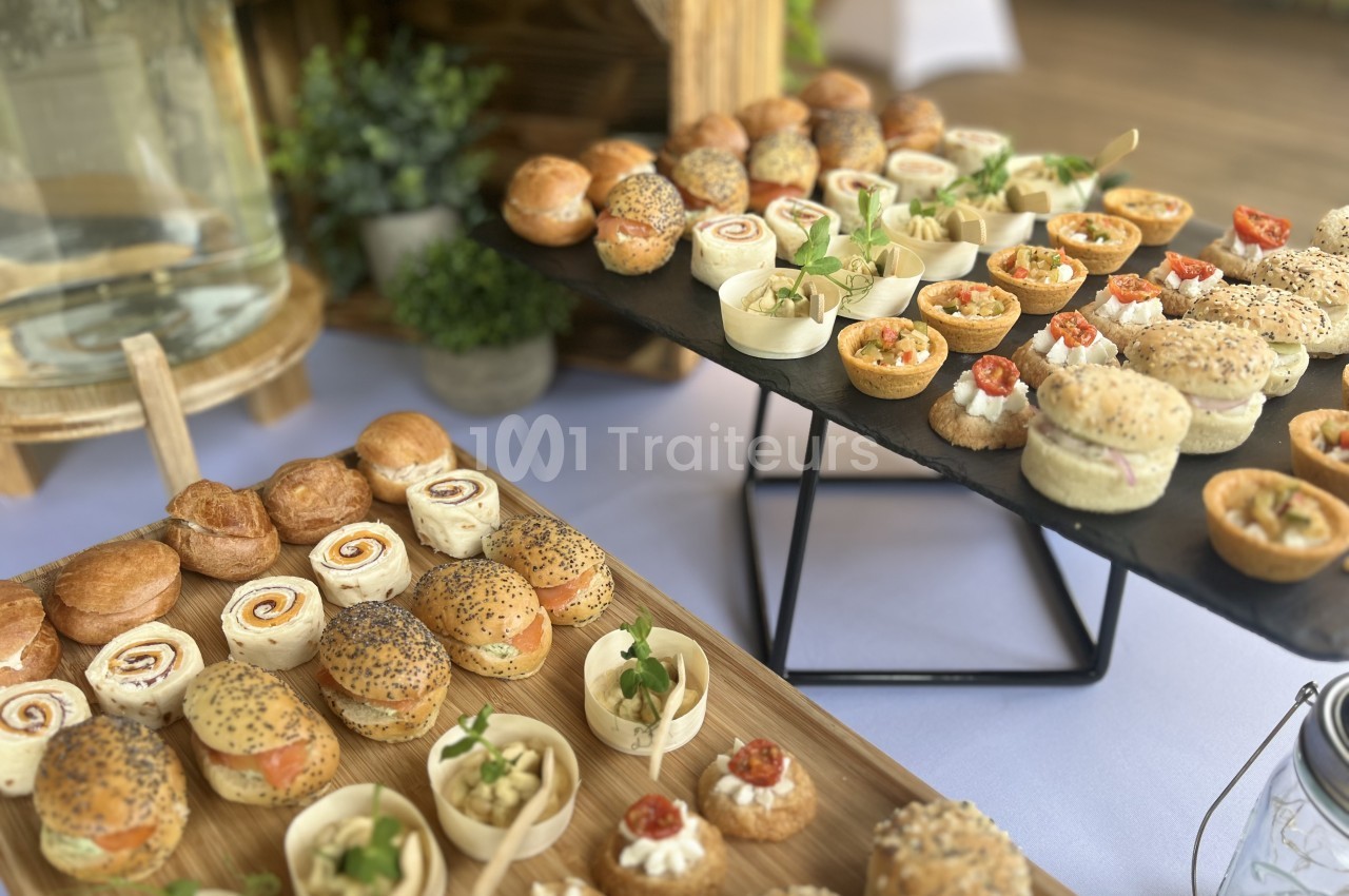 Traiteur La Petite Cuillère Traiteur Theix #1 Plateaux de cocktail dînatoire : mini-sandwichs ronds garnis de saumon, roulés de tortilla, bouchées en coupelles et tartelettes garnies, sur planches en bois et ardoise.