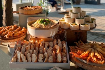 Buffet en plein air avec pain, houmous, crevettes frites et amuse-bouches présentés sur des plateaux en bois.