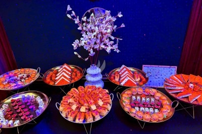 Plateau de desserts variés disposés sur des présentoirs, avec une décoration florale centrale et un éclairage coloré.