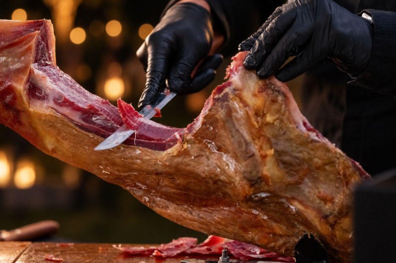 Mains gantées découpant au couteau une viande rôtie sur fond d'éclairage chaleureux.