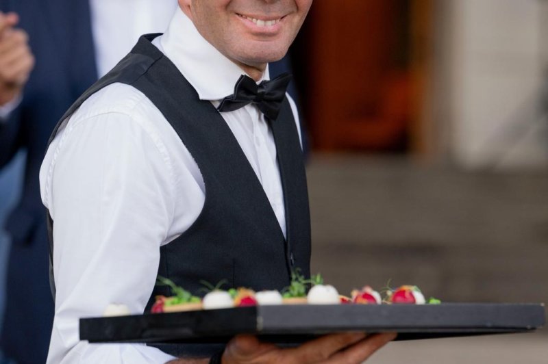 Serveur en tenue formelle tenant un plateau de canapés lors d'un événement.