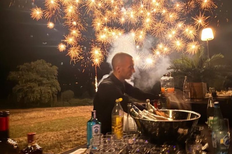 Feu d'artifice doré au-dessus d'une table dressée en plein air avec verres et bouteilles.