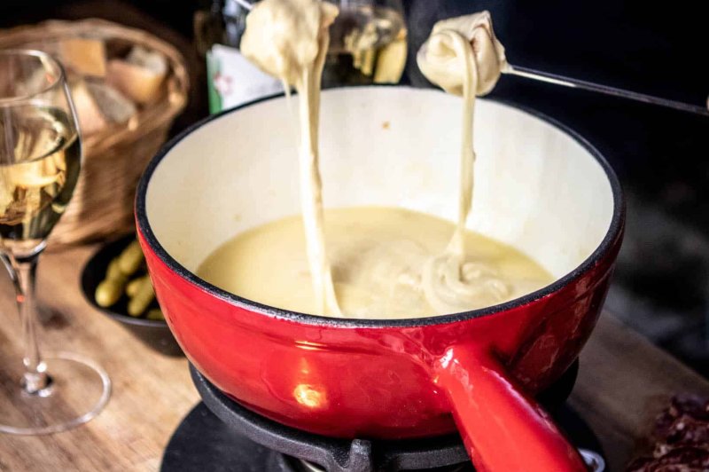 Traiteur Le 17.45 Vieux Lille Lille #3 Caquelon à fondue savoyarde rouge et blanc avec fromage fondu et deux fourchettes, accompagné de verres de vin blanc.